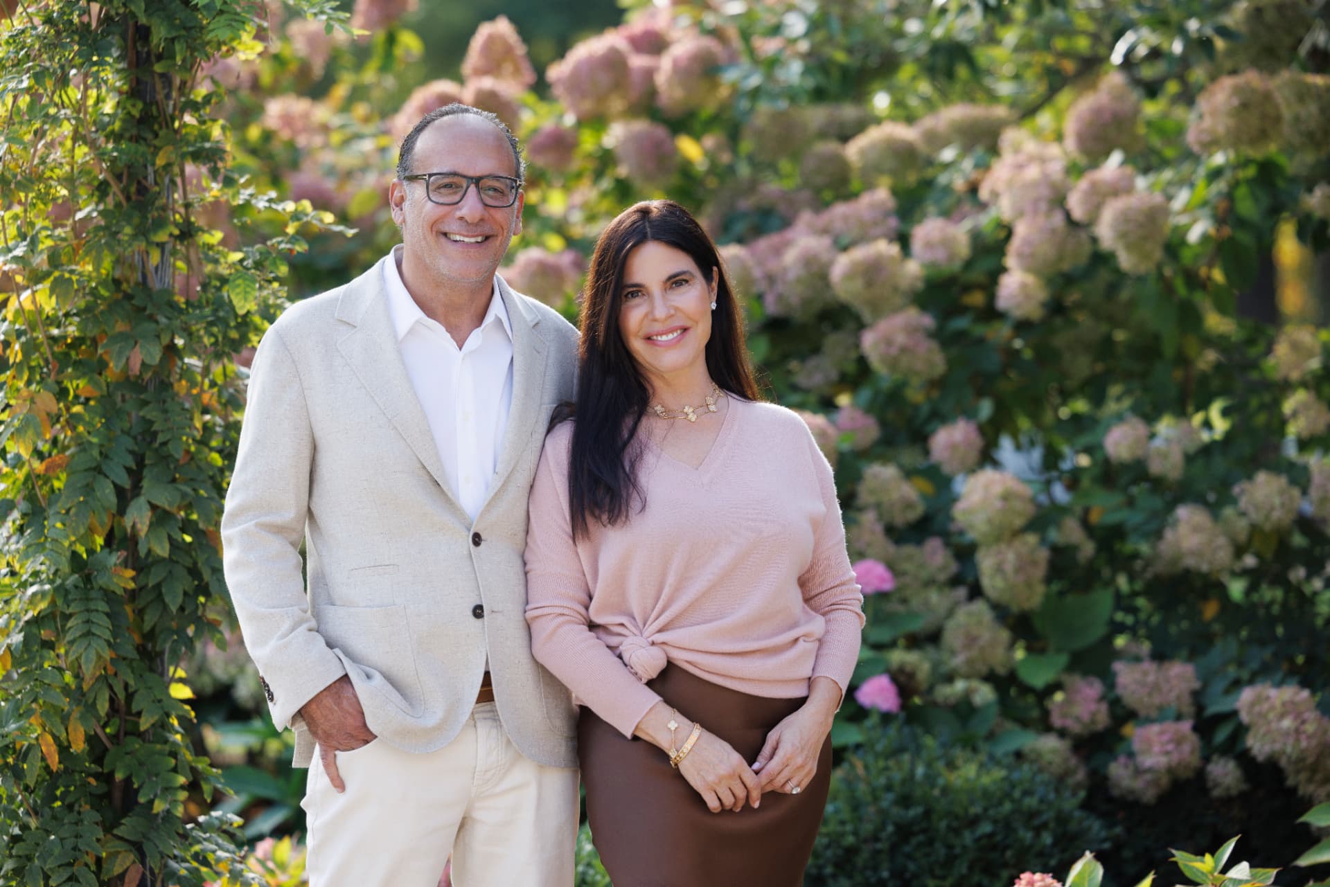 Sara and Rick Mershad standing together in a garden of hydrangeas